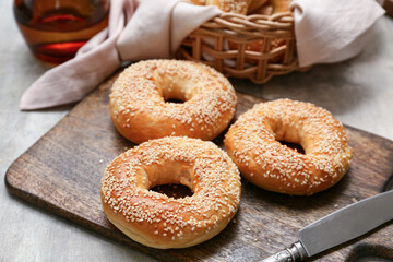 Wooden board of tasty bagels with sesame seeds on grey background, closeup