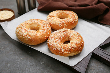 Wooden board of tasty bagels with sesame seeds on black background
