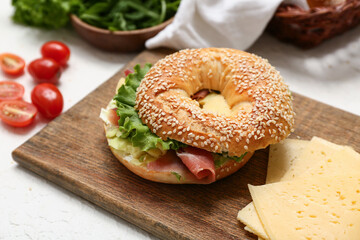 Wooden board of tasty bagel sandwich with prosciutto and cheese on white background