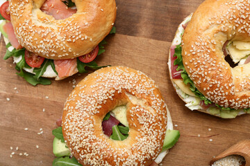 Tasty bagel sandwiches with ingredients on wooden background