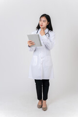 Serious, thoughtful Asian female doctor stands against a studio background with a tablet in her hand