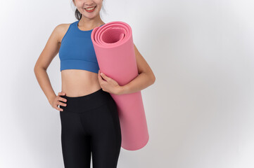 A confident, sporty Asian woman in sportswear holding her yoga mat against a white studio background