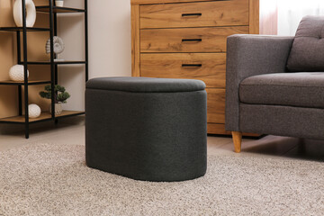 Black pouf, chest of drawers and armchair in interior of living room. Closeup