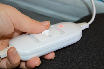 hand holding white electrical controller red indicator light bed mattress floral bedding wallpaper...