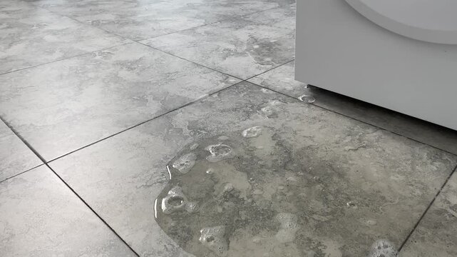 Water with detergent flows out from the bottom of the washing machine onto the floor.