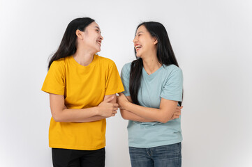 Two cheerful Asian female friends standing on a studio background, enjoying talking and laughing.