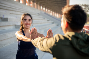 A cheerful Asian female in sportswear gives high five to her friend after exercising.