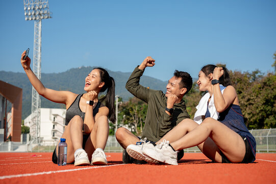 Group of athlete friends enjoying taking selfies while resting on a sports track after training.