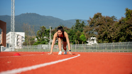 A determined woman sprinter in the starting position, ready to race on a racetrack at a stadium.