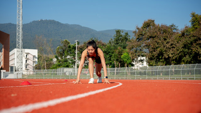 A determined woman sprinter in the starting position, ready to race on a racetrack at a stadium.