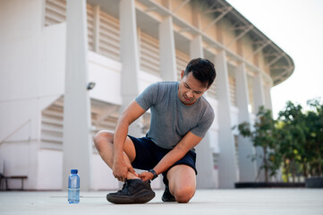 An Asian man in sportswear suffers a sprained ankle while running outdoors.