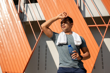 A tired, sweaty Asian man in sportswear, exhausted from running outdoors on a hot, sunny day.