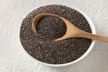 Bowl and wooden spoon with chia seeds on white background