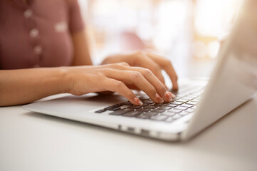 A woman working on her laptop computer, typing on the laptop keyboard, sitting in a cafe.