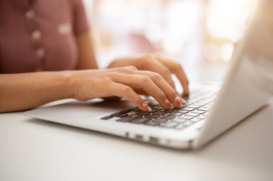 A woman working on her laptop computer, typing on the laptop keyboard, sitting in a cafe.