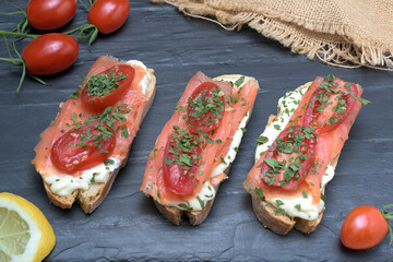 Salmon canape with tomato, cheese and lemon slice on black slate background