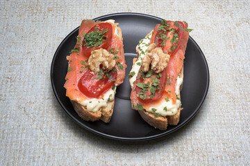 Salmon canap&eacute; with tomato, cheese, walnuts on black plate on rustic background