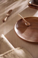 Various tableware on a soft wood-toned table background with sunlight shining through.