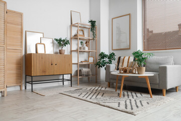 Cozy sofa, coffee table and chest of drawers with blank posters in interior of living room