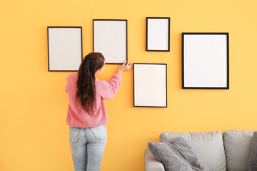 Woman hanging blank photo frames on wall in room