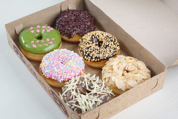 six donuts topped with strawberry chocolate matcha and tiramisu in a paper box photographed with studio lighting
