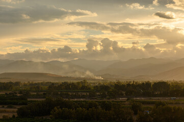 Majestic sunset over rolling hills with wisps of smoke rising in the distance