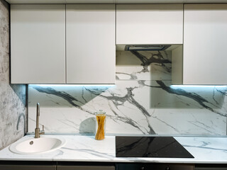 This is a stylish kitchen that features elegant white cabinets, a functional sink, a modern stove, and a stunning marble counter top, making it both beautiful and practical