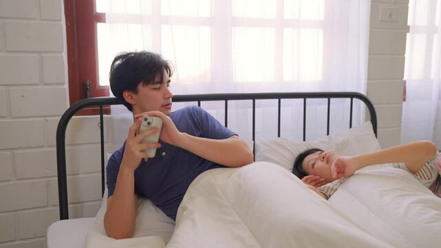Asian man secretly chatting to mistress while lying in bed with girlfriend.