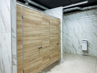A public restroom featuring elegantly designed wooden stalls complemented by luxurious marble walls, creating an inviting atmosphere for users. The overall design reflects modern aesthetics