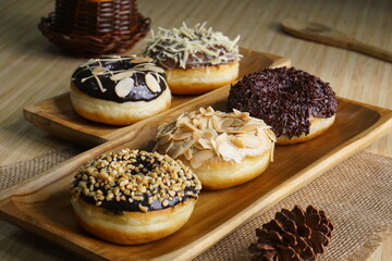 several donuts with chocolate topping, tiramisu, peanut cheese and sprinkles, on a wooden base, photographed with studio light with a wooden theme
