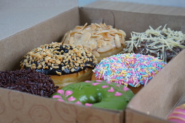 six donuts topped with strawberry chocolate matcha and tiramisu in a paper box photographed with studio lighting