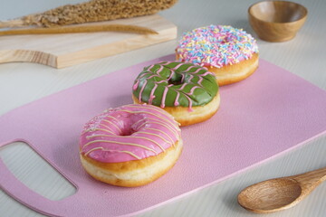 three donuts with strawberry matcha topping and sprinkles, on a pink plastic plate photographed with studio light