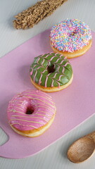 three donuts with strawberry matcha topping and sprinkles, on a pink plastic plate photographed with studio light