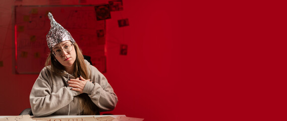 Woman wearing glasses in foil hat showing heart love emotion putting hands on chest sitting on red...