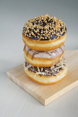 three medium sized donuts topped with chocolate sprinkles, tiramisu nuts and cheese, stacked together, on a wooden board photographed with studio light
