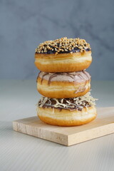 three medium sized donuts topped with chocolate sprinkles, tiramisu nuts and cheese, stacked together, on a wooden board photographed with studio light