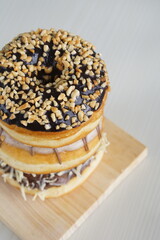 three medium sized donuts topped with chocolate sprinkles, tiramisu nuts and cheese, stacked together, on a wooden board photographed with studio light