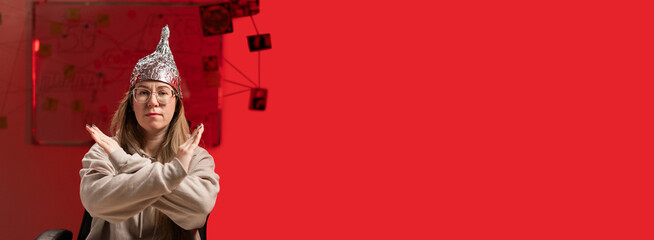 Woman wearing glasses in foil hat showing stop, no, ban gesture, sitting on red background....