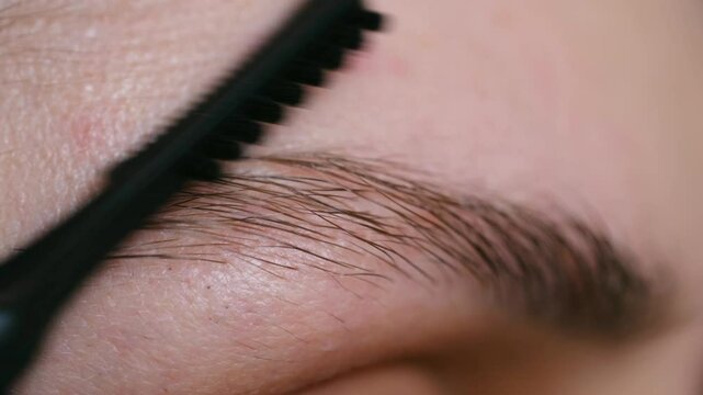 Close-up beauty shot of a caucasian woman combing her eyebrows with a modern mascara brush, enhancing her natural beauty and achieving a polished look