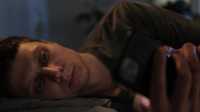 Man scrolls through his phone at night in bed, losing sleep due to social media and fast-paced video content.
