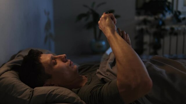 Man scrolling phone in bed at night, leading to irritation and sleep problems.