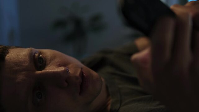 Man scrolling on phone in bed at night, unable to sleep. Close-up