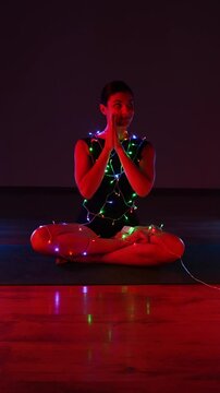 Woman meditating in a Christmas atmosphere with yf garlands on her body. Christmas yoga. Christmas concept. Vertical video 4k