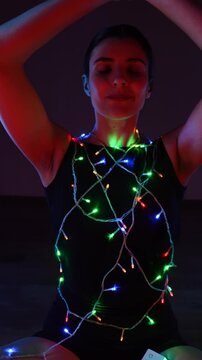 Woman meditating in a Christmas atmosphere with yf garlands on her body. Christmas yoga. Christmas concept. Vertical video 4k