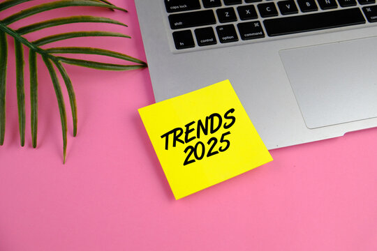 text of TREND 2025 on the plain yellow sticker note and laptop. business concept on pink background.