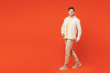 Full body young smiling happy cheerful satisfied man he wear white shirt yellow t-shirt casual clothes walk go look camera isolated on plain red orange background studio portrait. Lifestyle concept.