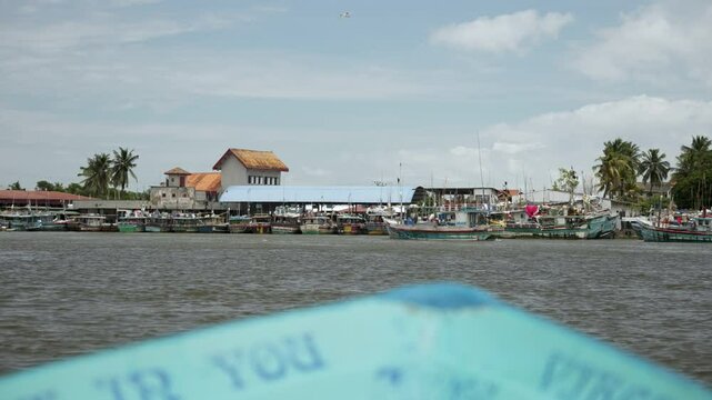 Colorful bow of a boat navigating on negombo lagoon with religious inscriptions, featuring a bridge and docked boats in the background, sri lanka