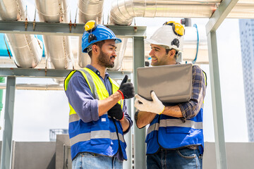 Collaboration, Two young construction workers discuss plans and use laptop computer while reviewing...