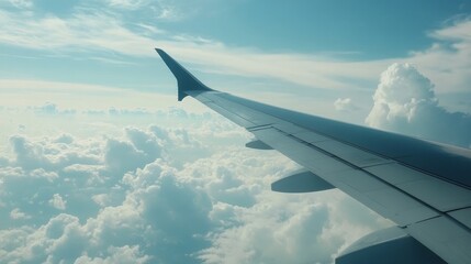Obraz premium The wing of an airplane gracefully soars through the clouds, showcasing the airplane s wings against a backdrop of blue sky and fluffy white clouds. Witness the beauty of the airplane in flight.
