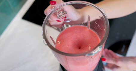 Woman Blending Smoothie with Strawberries and Bananas in Kitchen